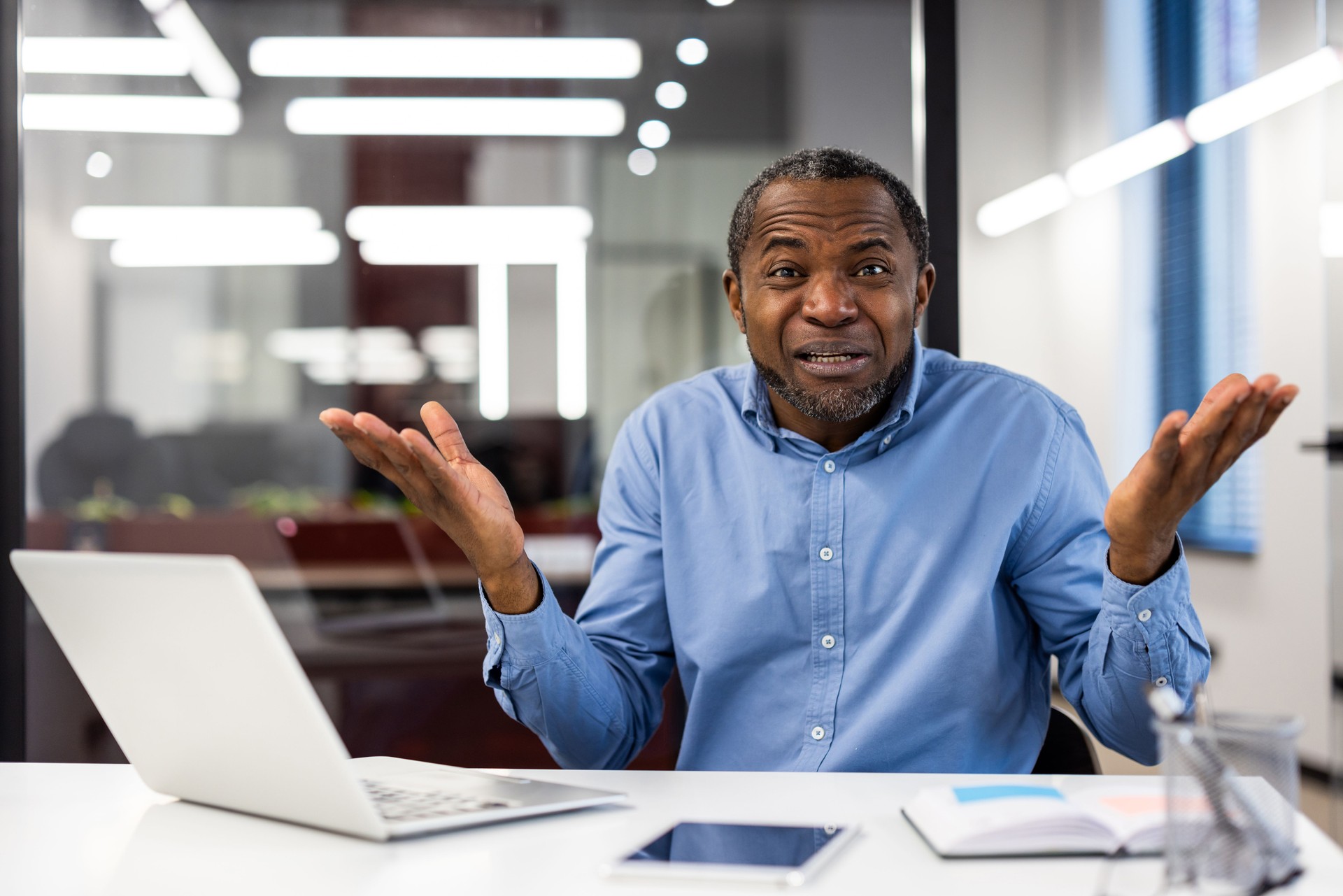 Confused businessman with open arms explaining issue in modern office