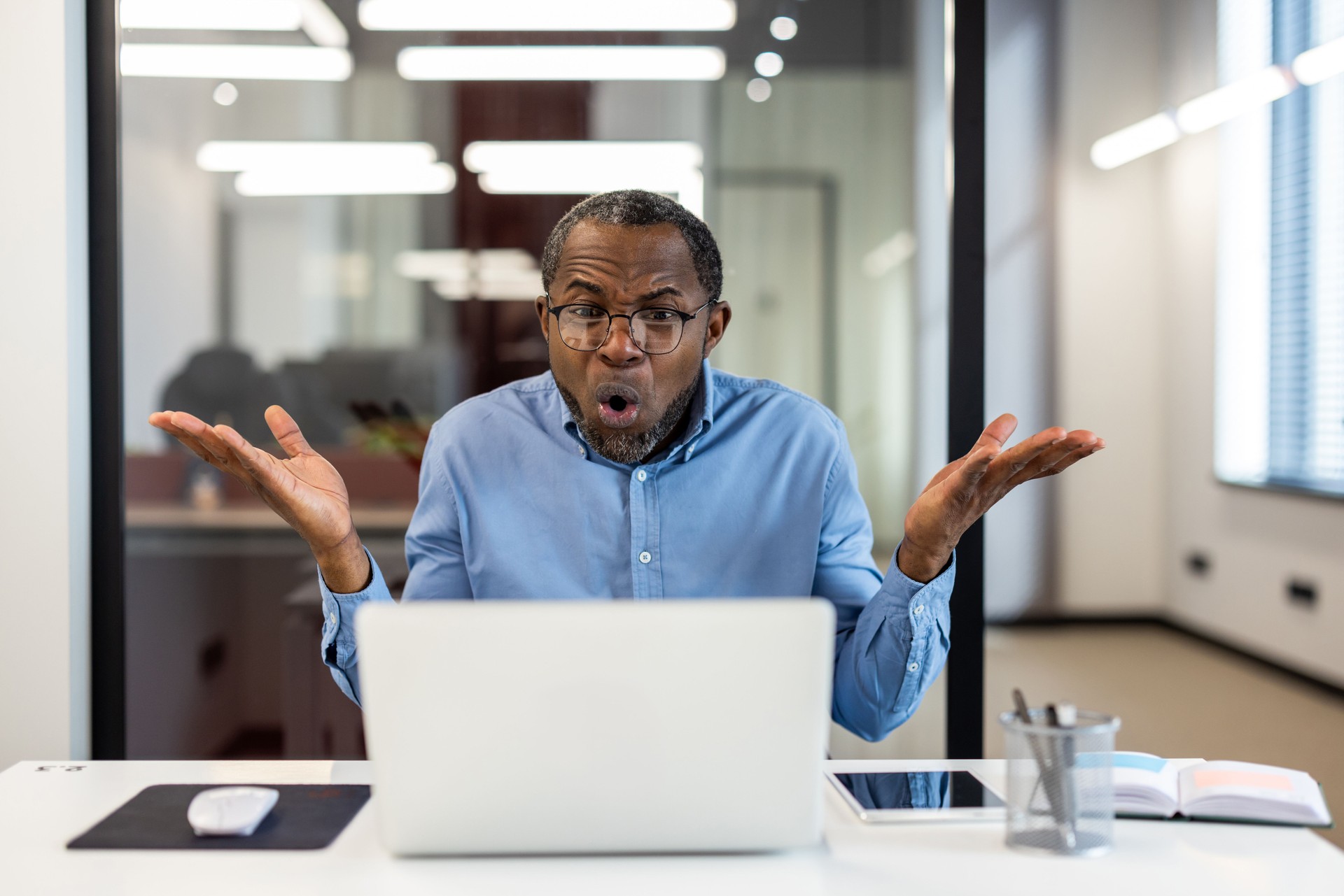 Surprised businessman in office gesturing at laptop screen in modern workspace
